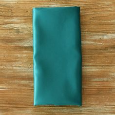 a plain teal green pocket square on a wooden table with wood grains in the background