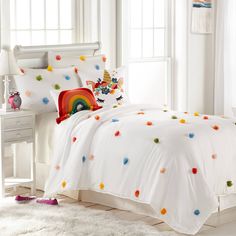 a bed with white sheets and colorful polka dots on the comforter is in front of a window