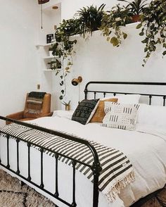 a bed with white sheets and black iron frame, plants on the wall above it