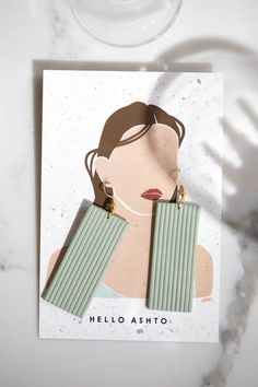 a greeting card with an illustration of a woman's face and two green striped earrings