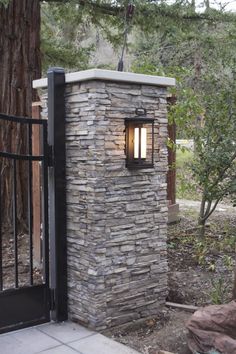 an outdoor light that is on the side of a stone wall in front of a gate