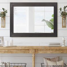 a mirror on the wall above a wooden table with baskets and plants in front of it