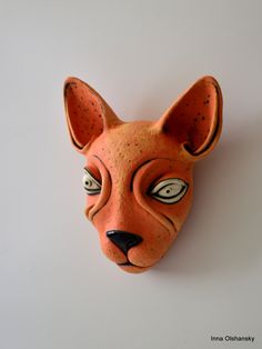 an orange cat mask with eyes on it's face is hanging on the wall