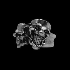 a silver ring with two skulls and a ball on it's face, against a black background