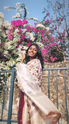 a woman standing next to a fence with flowers on it and holding a scarf over her shoulder