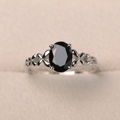 a black diamond engagement ring on a white surface with an intricate design around the band