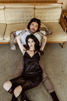 a man and woman laying on the floor in front of a couch with tattooed arms