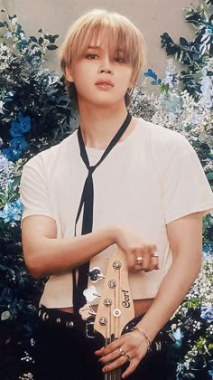 a young man holding a wooden guitar in front of some blue and white flowers,