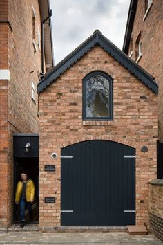 two people walking into a brick building with a large black garage door and arched window