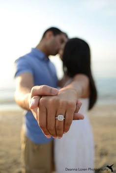 a man and woman holding hands on the beach with their fingers pointing towards the camera