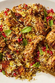 a white plate topped with rice and meat covered in pomegranates, garnished with green leaves