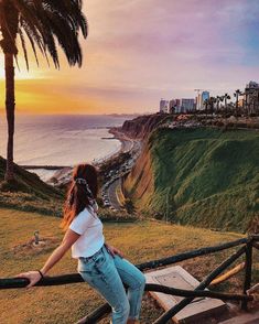 a woman standing on top of a wooden railing next to the ocean and palm trees