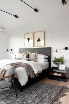 a bedroom with white walls and wooden floors, two framed pictures on the wall above the bed