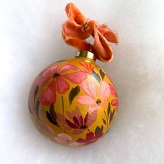 an ornament with flowers painted on it sitting on a white table top next to a red flower