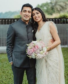 a man and woman standing next to each other in front of a fence with flowers