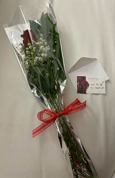 a bouquet of flowers wrapped in cellophane and tied with a red ribbon on a bed