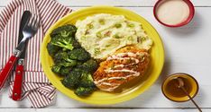 a yellow plate topped with meat, mashed potatoes and broccoli covered in sauce