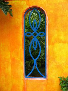 an orange wall with a blue window and plants in the foreground on either side