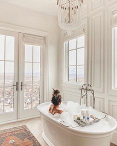 a woman in a bathtub surrounded by windows and a chandelier hanging from the ceiling