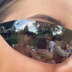 a woman wearing mirrored sunglasses with her reflection in the lens, and people behind her