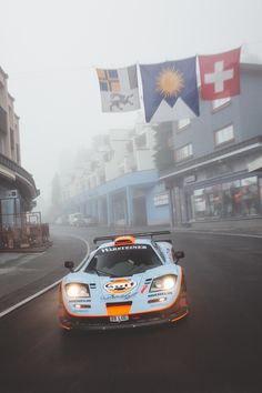 a race car driving down the road in front of some buildings on a foggy day