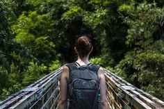 a woman walking across a bridge with a backpack on her back and trees in the background