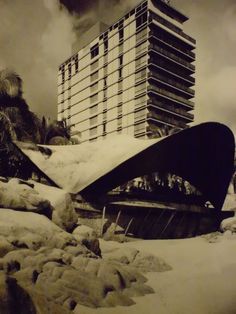 a very tall building sitting in the middle of a snow covered field next to rocks