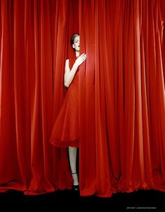 a woman standing in front of red curtains with her hand on the curtain's edge