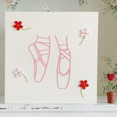 a handmade card with pink shoes and flowers on the front, sitting next to a potted plant