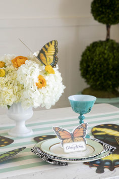 there is a vase with flowers and two butterflies on the table next to each other