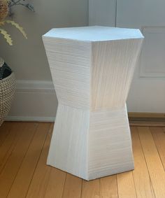 a white vase sitting on top of a hard wood floor next to a planter