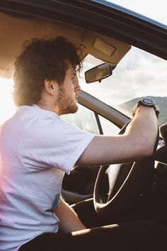 a man sitting in the driver's seat of a car with his hand on the steering wheel