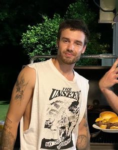 a man standing in front of an open grill holding a plate of food and pointing at the camera