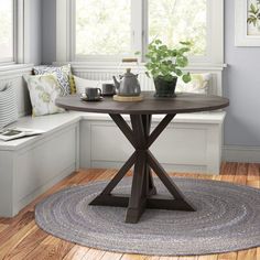 a round table with two vases on it in front of a window and bench