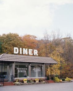 an old diner sits in the middle of a parking lot with autumn trees around it