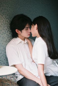 a man and woman sitting next to each other in front of a wallpapered room