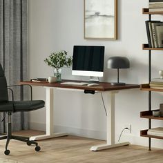 a desk with a computer on it in front of a bookshelf and window