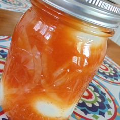 a jar filled with orange liquid sitting on top of a colorful table cloth next to a metal lid