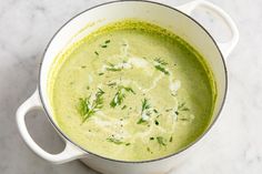 a white pot filled with green soup and garnished with fresh dill sprigs