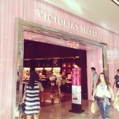 people walking in front of a store with pink walls and glass doors that say victoria's secret