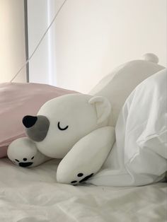 a large white teddy bear laying on top of a bed under a pink pillow cover