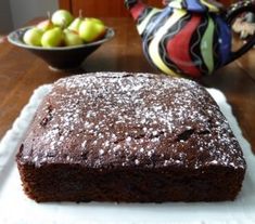 a brownie sitting on top of a white plate next to a bowl of fruit