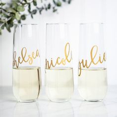 three wine glasses with gold lettering sitting on a white counter top next to a plant