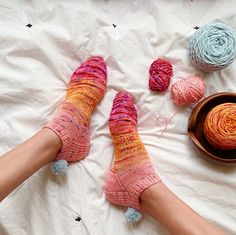 a person laying on a bed with their feet up next to balls of yarn and a bowl