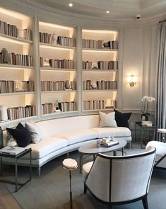 a living room filled with lots of white furniture and bookshelves full of books