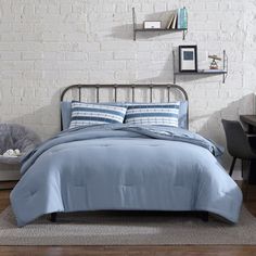 a bed with blue comforter and pillows in a room next to a brick wall