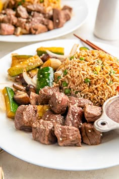 two plates with meat, rice and vegetables on them next to some chopsticks