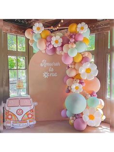 the balloon arch is decorated with flowers and an old vw campervan in pastel colors