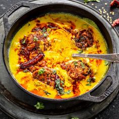 a pan filled with food on top of a black counter next to spices and herbs