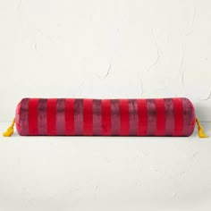 a red and pink striped pillow sitting on top of a white floor next to a wall